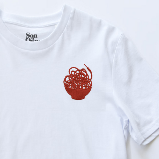 Close up of a white synth t-shirt showing a small red embroidered graphic of a messy noodle bowl overspilling with patching modular synth cables.