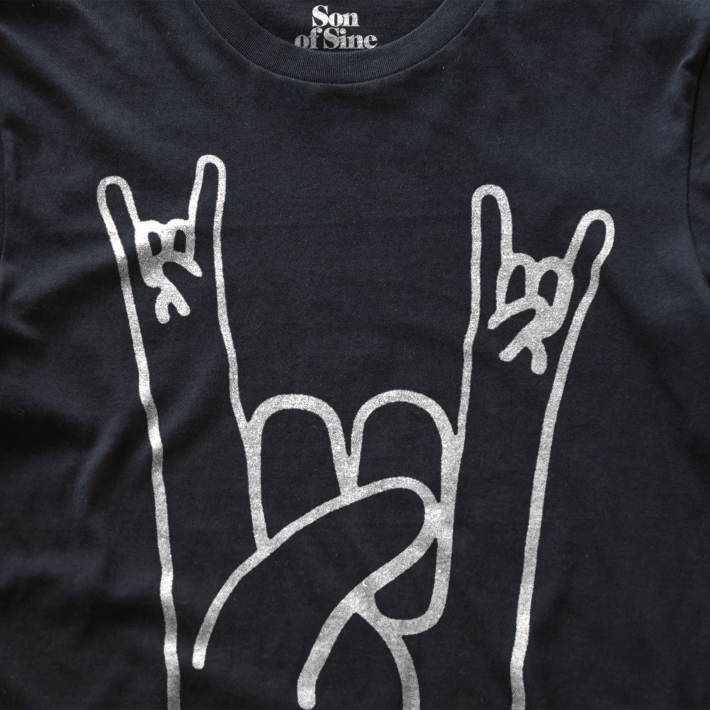 Close-up of a black music festival t-shirt featuring a white graphic of two hands making the rock on sign.