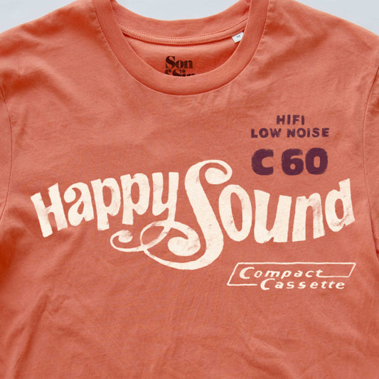 A close-up of a coral coloured synth inspired t-shirt featuring a vintage-style cassette sleeve graphic print that reads 'Happy Sound C60 HIFI LOW NOISE' and 'Compact Cassette'.