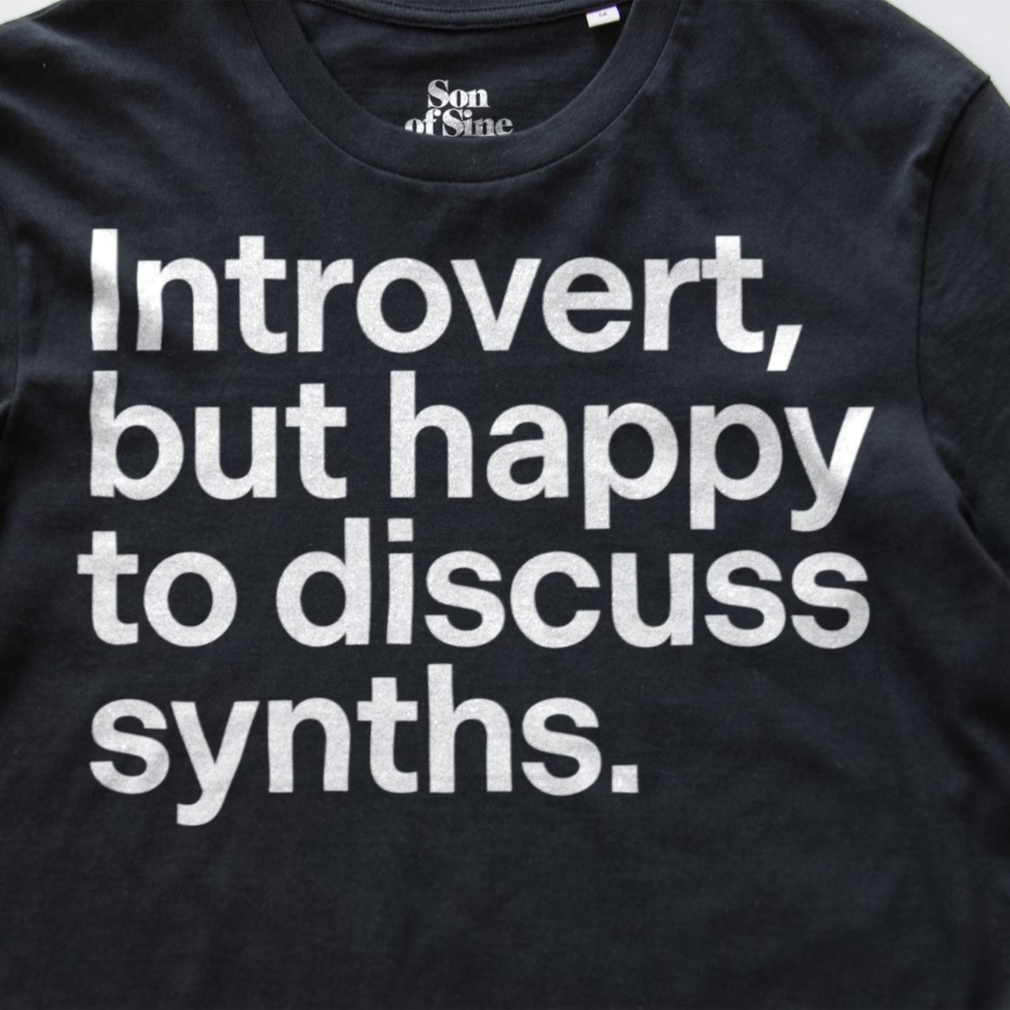 A detail image of a funny synth inspired t-shirt with bold white text reading 'Introvert, but happy to discuss synths.' printed on the front.