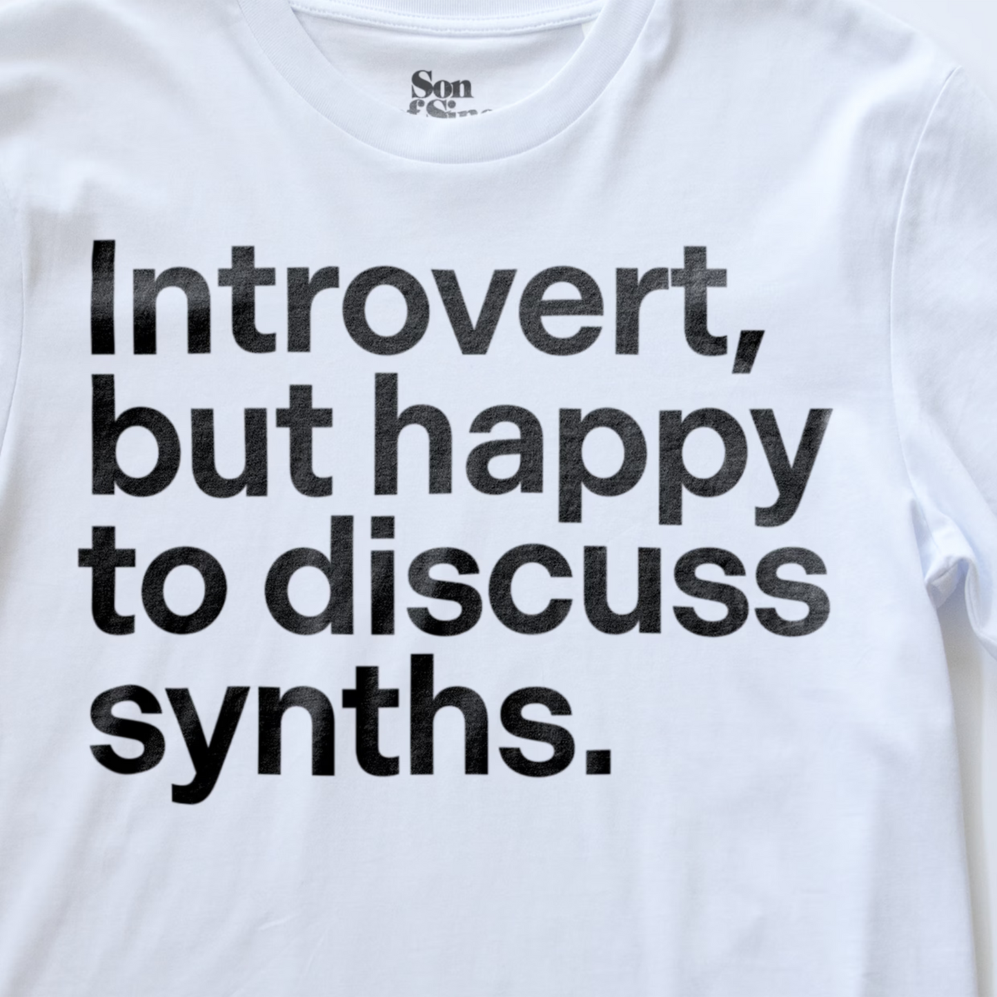 A close up of a funny synth inspired t-shirt with bold black text reading 'Introvert, but happy to discuss synths.' printed on the front.