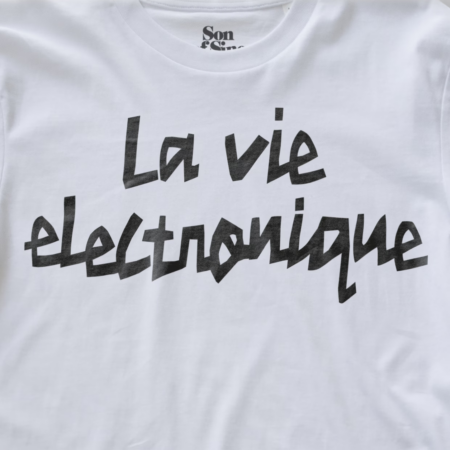 White synth t-shirt with 'La vie electronique' printed in a black brush-stroke style font across the chest.