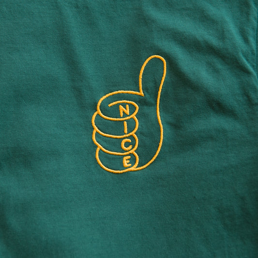 A close-up of a dark green synth t-shirt with a yellow embroidered graphic of a thumbs-up hand enclosing the word 'NICE'.