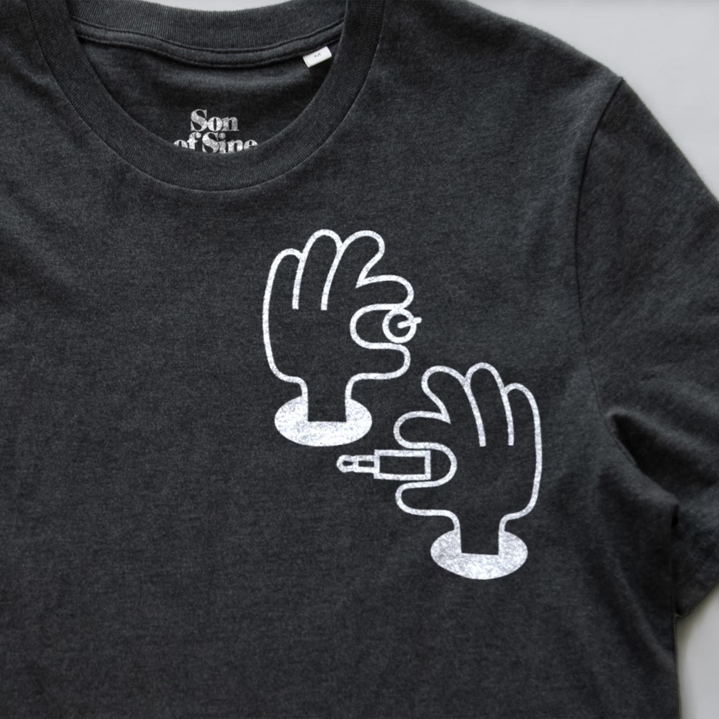A close-up of a synth inspired t-shirt featuring a white graphic print of two illustrated hands patching and tweaking.