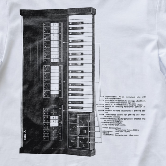 A close-up of a white synth T-shirt featuring a large black graphic print of a vintage synthesizer instrument with technical labels and notes printed alongside it.