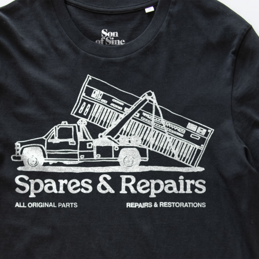 A close-up of a black electronic music t-shirt featuring a white graphic of a tow truck lifting a synth with the text 'Spares & Repairs' and 'All Original Parts Repairs & Restorations'. The inner collar shows the brand 'Son of Sine'.