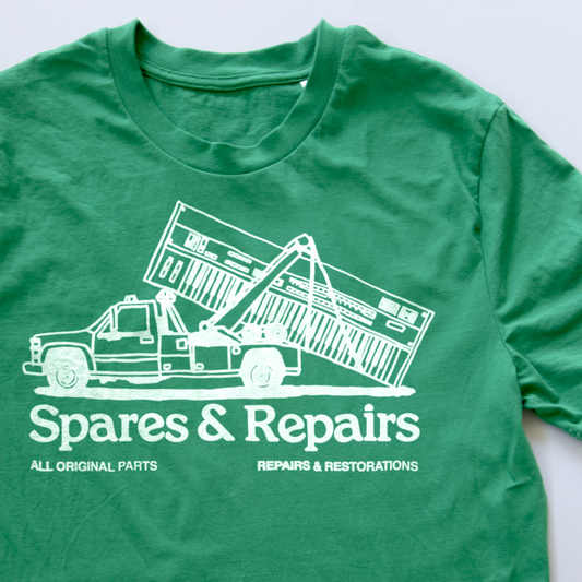 A green synth t-shirt featuring a white graphic of a tow truck lifting a synth, with the text 'Spares & Repairs' and 'ALL ORIGINAL PARTS REPAIRS & RESTORATIONS'.