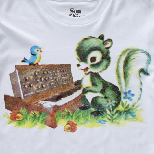 White synth t-shirt featuring a vintage-style graphic print of a green squirrel playing a brown minimoog synthesizer piano, with a small blue bird perched on the keyboard and grassy details.