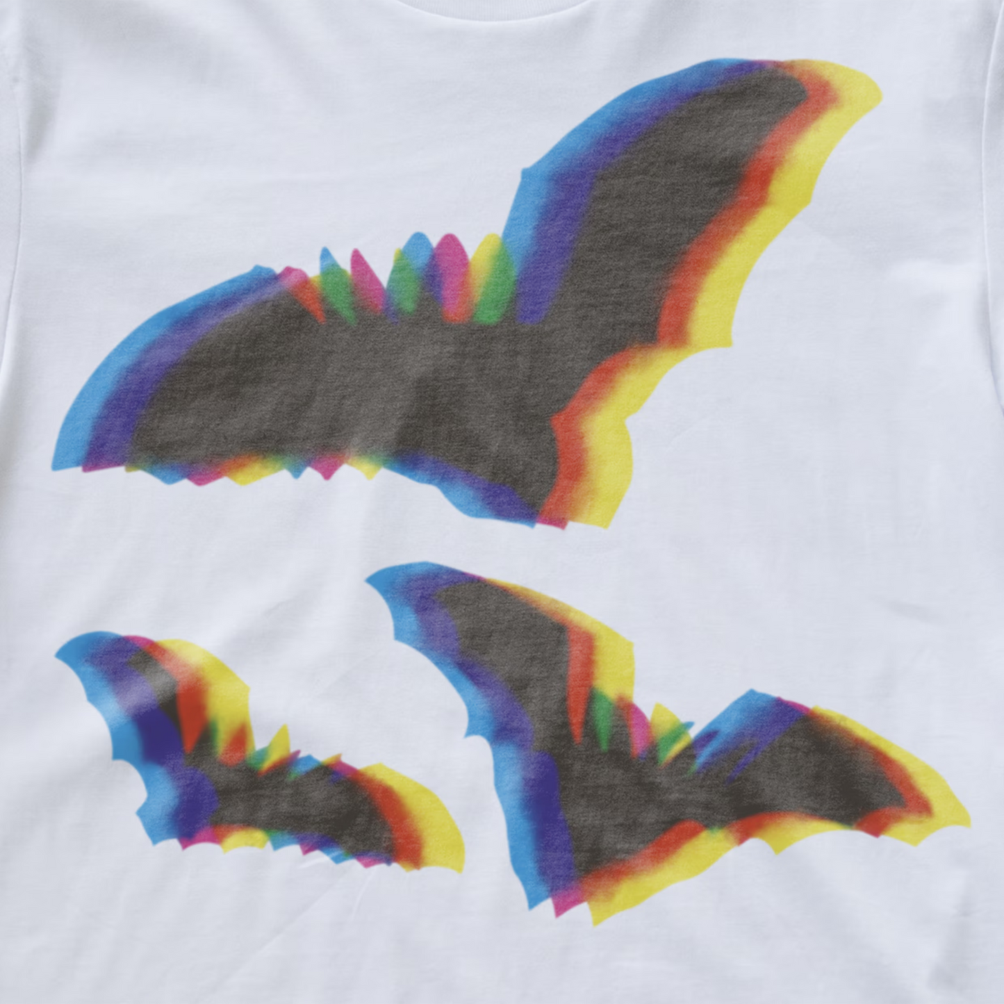 An electronic music T-shirt featuring three stylized bat wing graphics in a rainbow gradient, with the largest bat graphic on the chest and two smaller ones below.