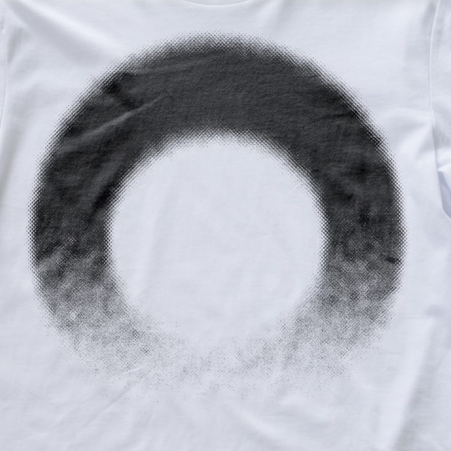 A close-up of a white modular synth t-shirt featuring a large, circular black halftone dot pattern that fades into a solid white center.