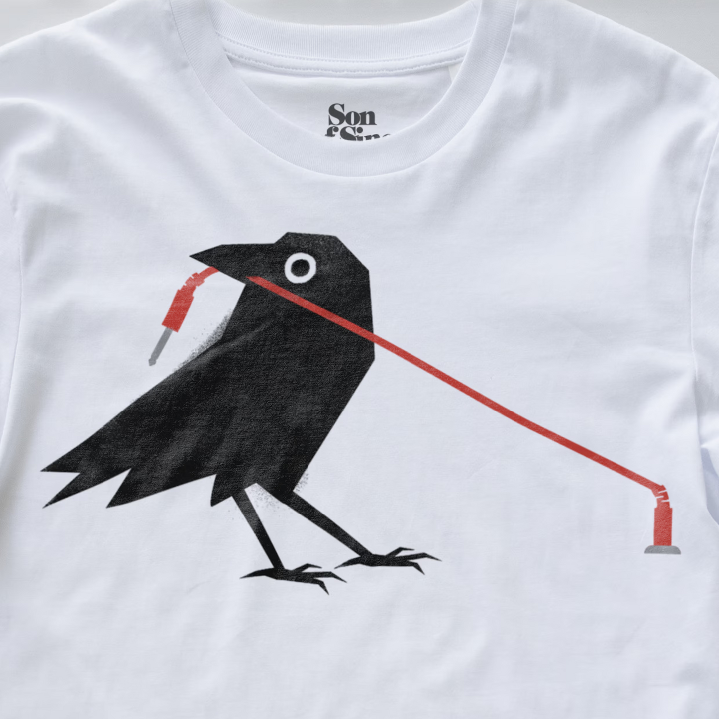 A close up of a modular synth t-shirt featuring a graphic print of a black crow holding a red patching cable in its beak.