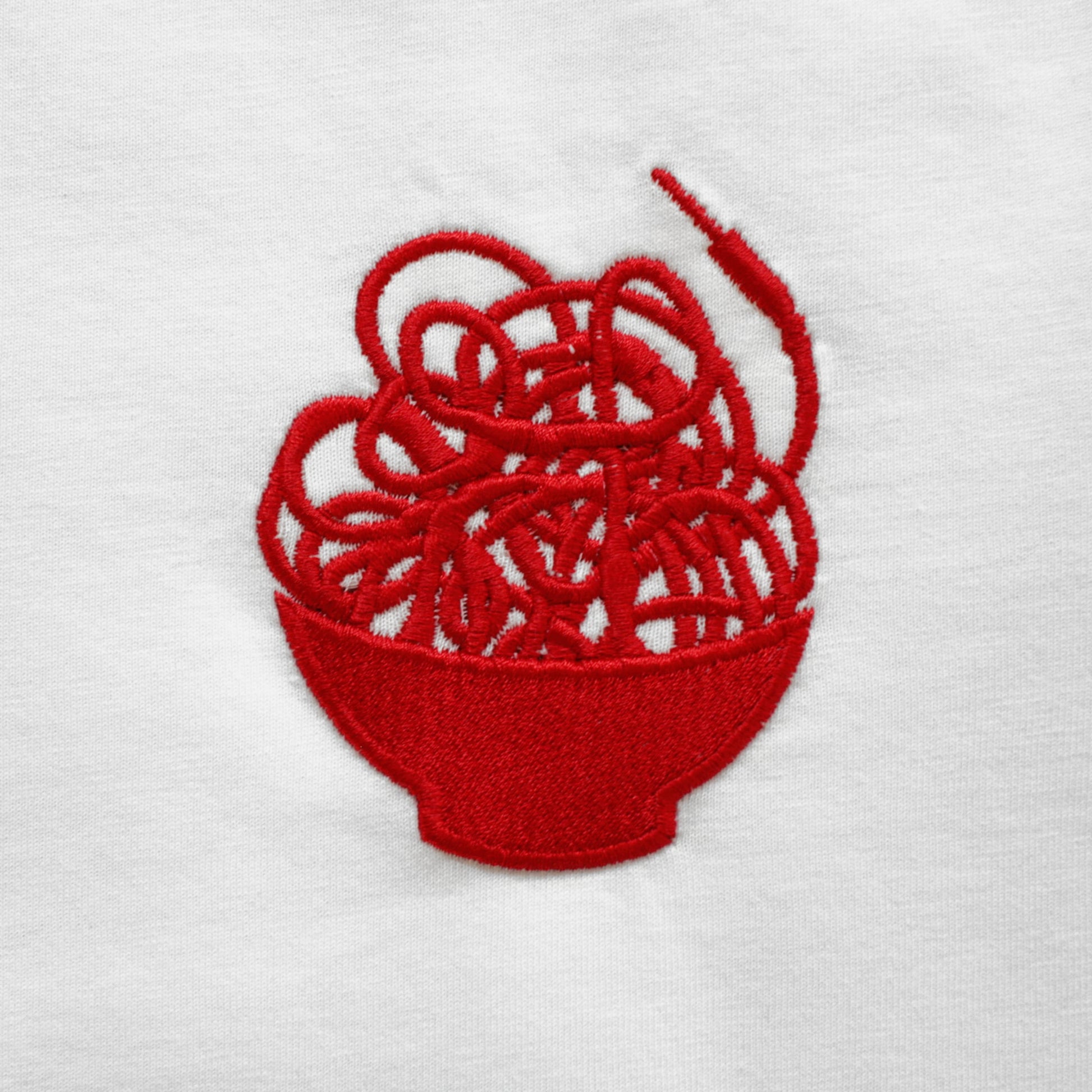 A close-up of a red embroidered graphic of a messy noodle bowl overspilling with patching modular synth cables.