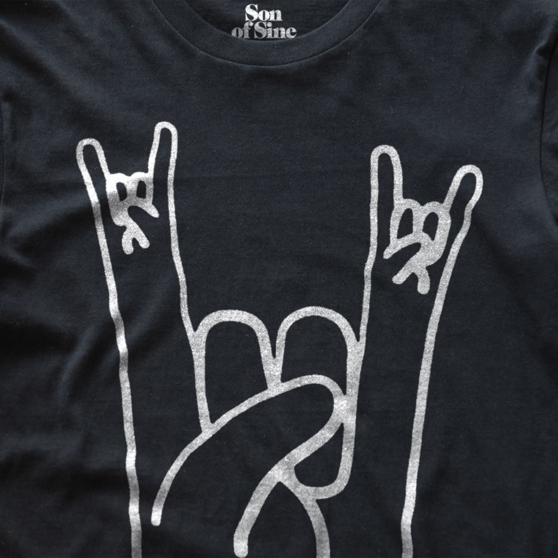 Close-up of a black music festival t-shirt featuring a white graphic of two hands making the rock on sign.