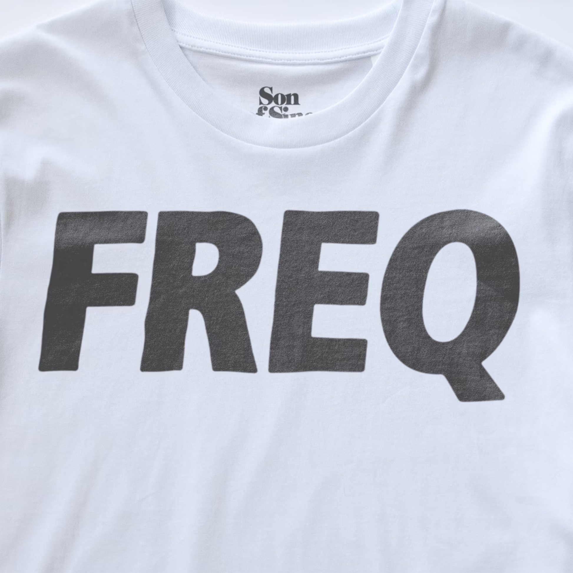 White electronic music club wear t-shirt featuring the word 'FREQ' printed in large, bold, dark gray block letters across the chest. The inner collar shows the 'Son of Sine' brand logo.