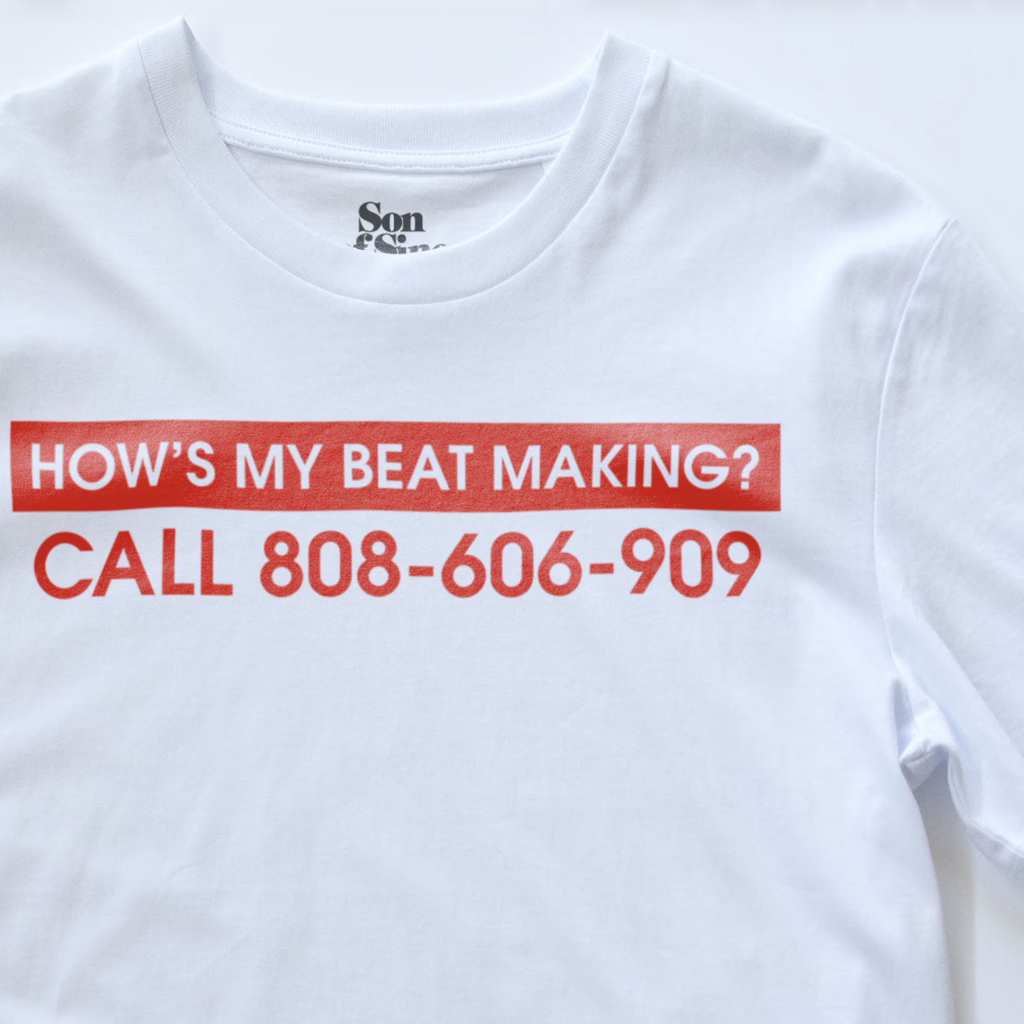 Close up of a synth inspired t-shirt with a red graphic print that reads 'HOW'S MY BEAT MAKING? CALL 808-606-909'. The inner collar shows the 'Son of Sine' brand logo.