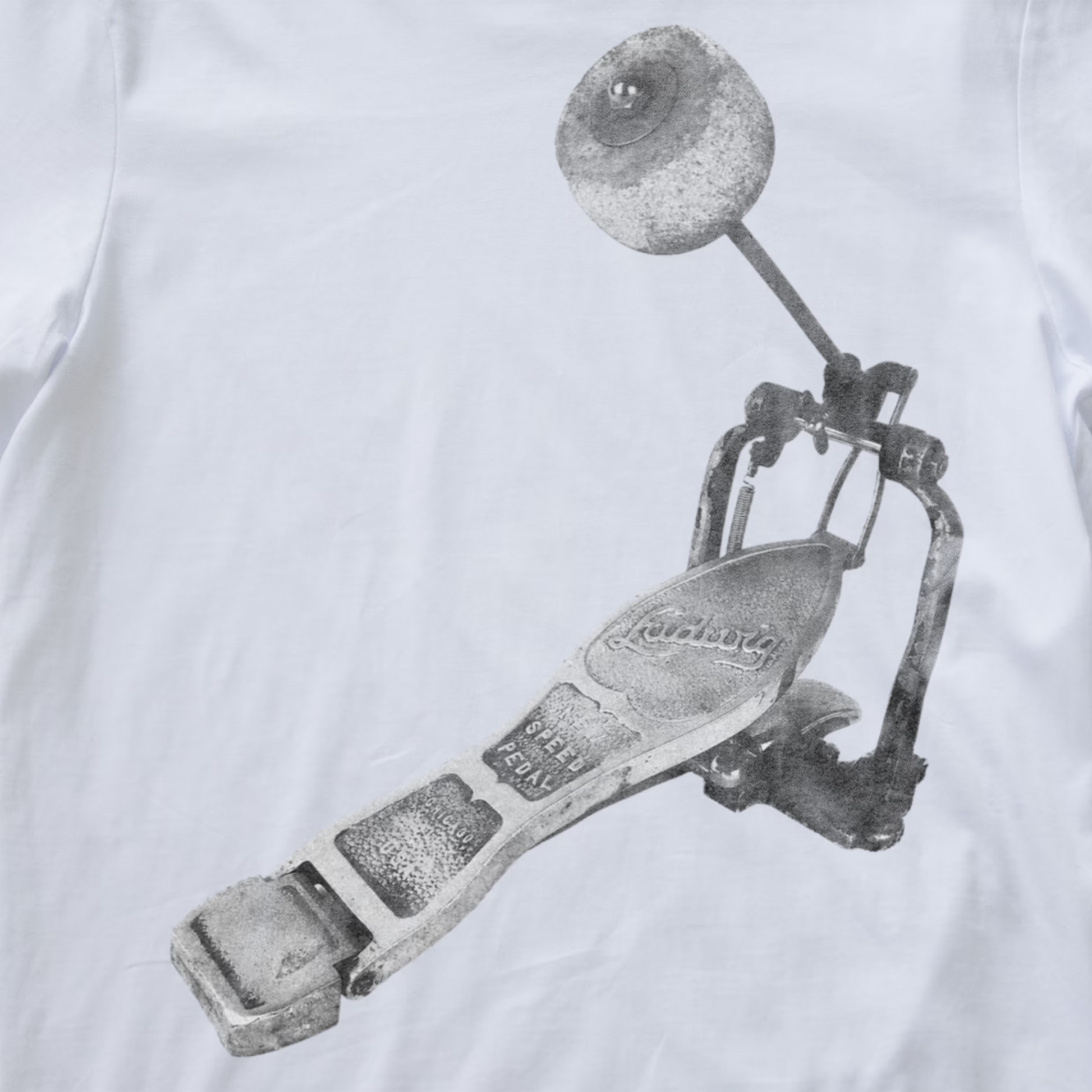 A close-up of a white fabric surface featuring a large grayscale printed graphic of a metal drum pedal.