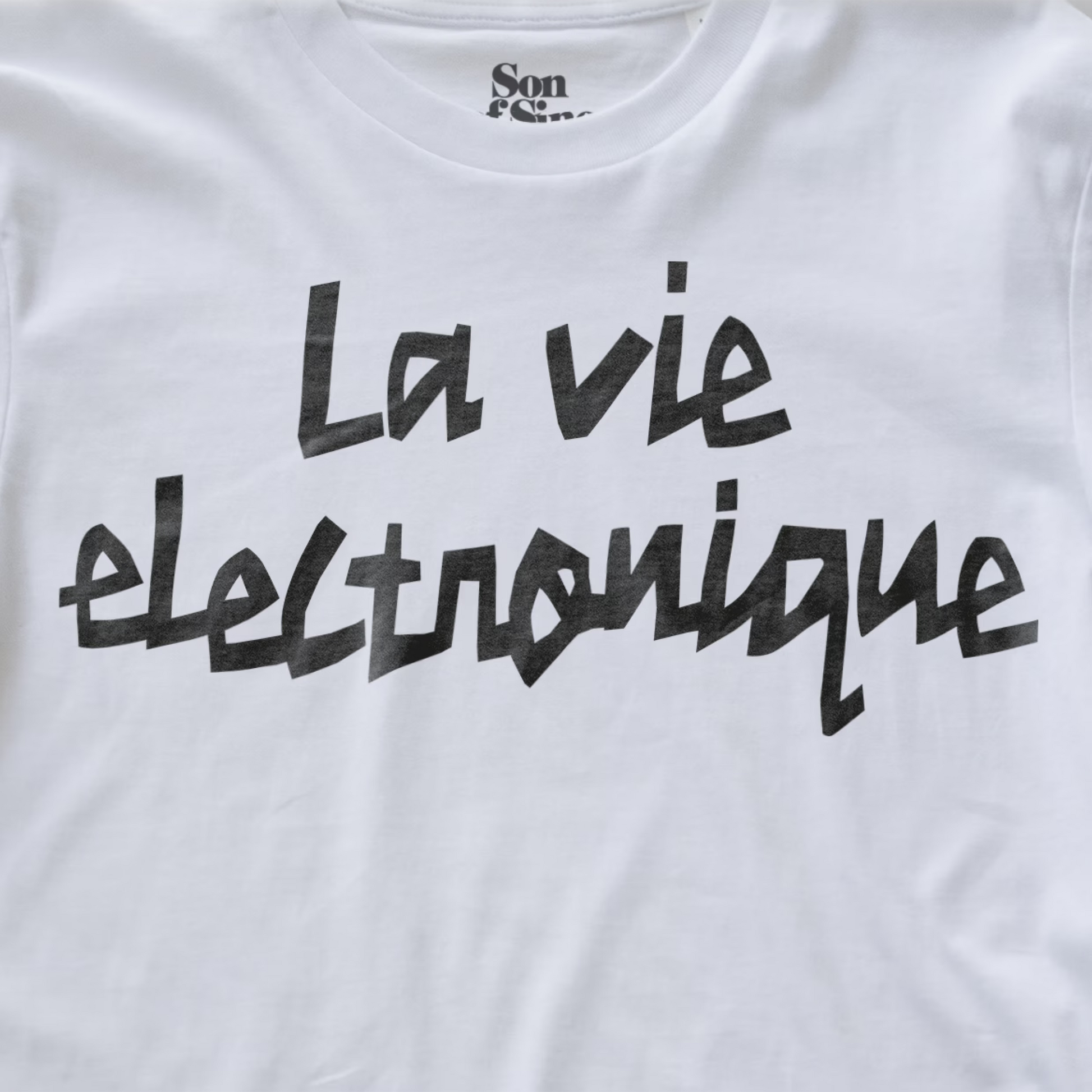 White synth t-shirt with 'La vie electronique' printed in a black brush-stroke style font across the chest. 