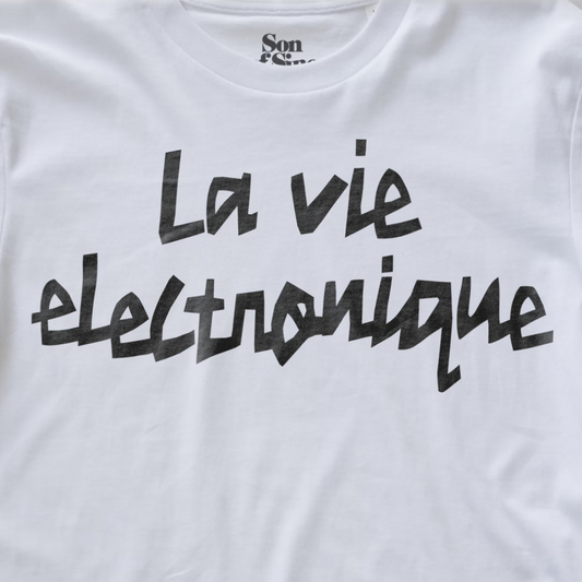 White synth t-shirt with 'La vie electronique' printed in a black brush-stroke style font across the chest. 