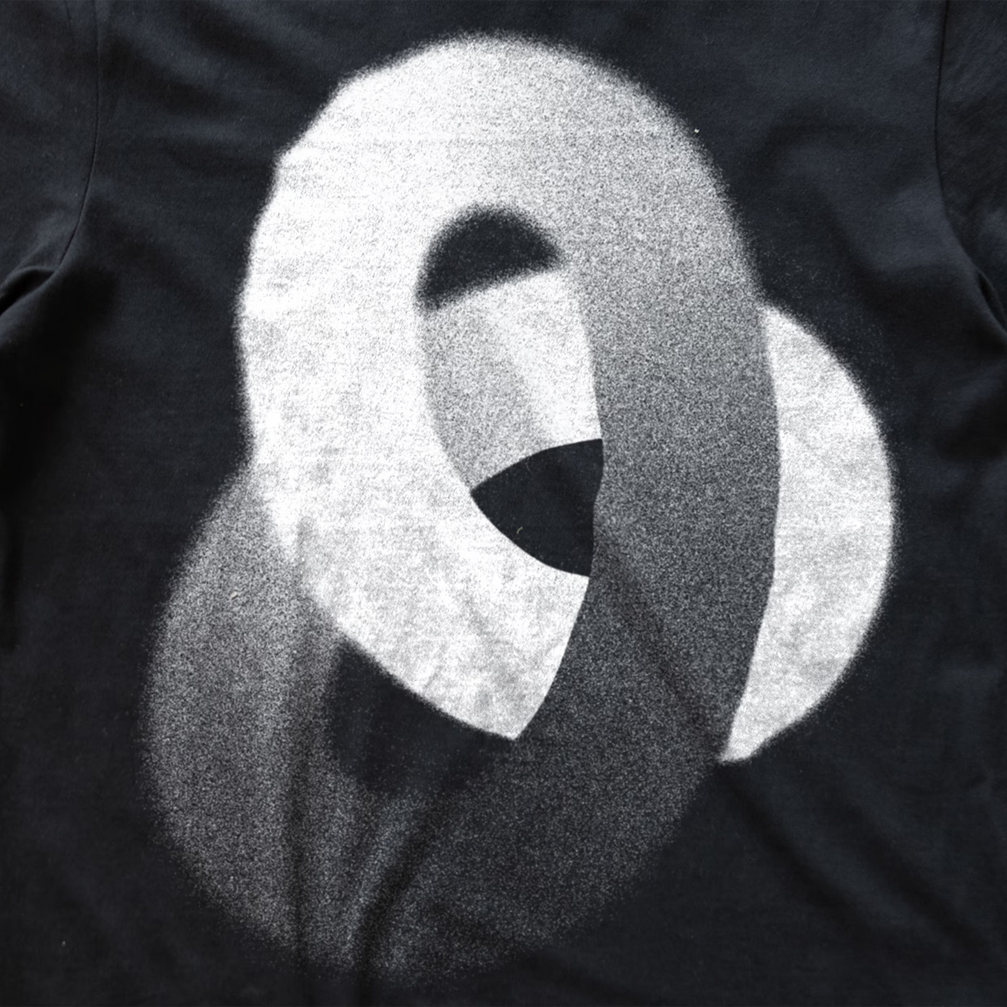 A close-up of a black synth t-shirt featuring a large, textured white graphic print of an abstract interlocking looping design.