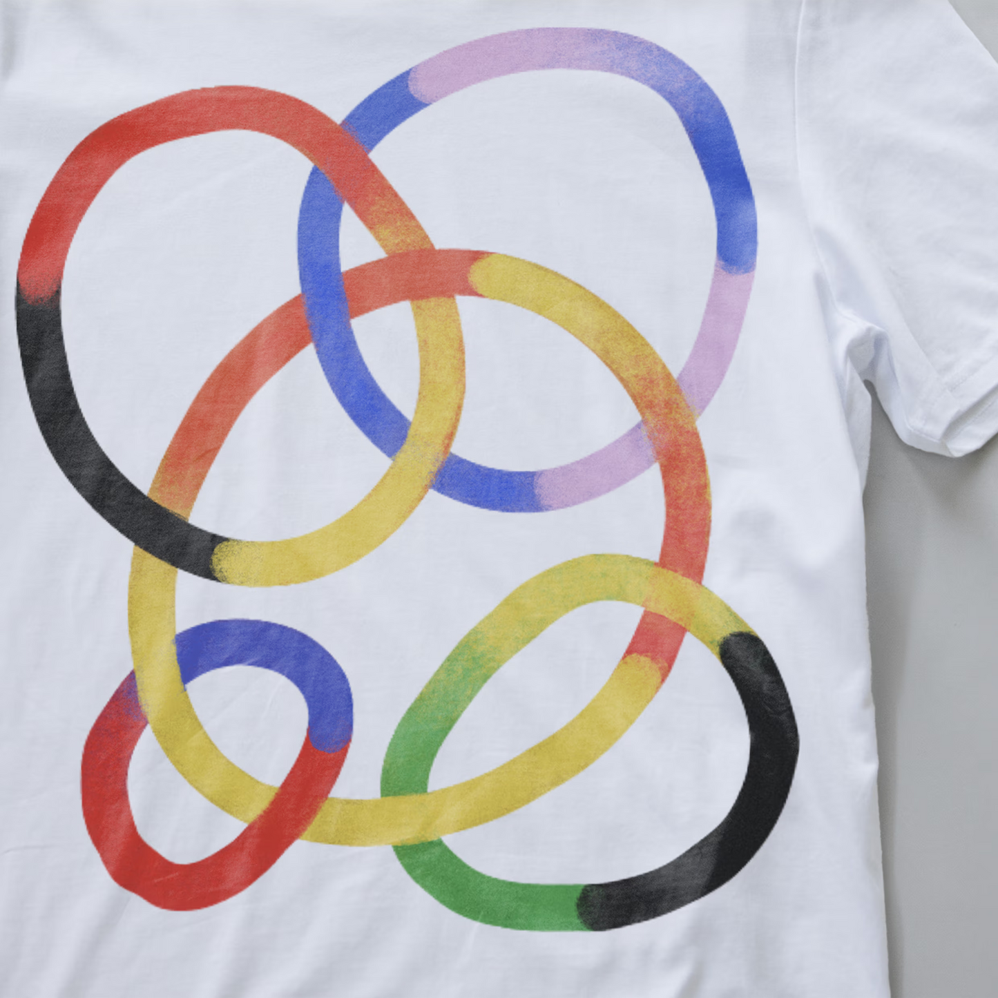 Close up of a white electronic music festival t-shirt featuring a graphic of overlapping watercolor-style rings in red, yellow, blue, purple, green, and black.