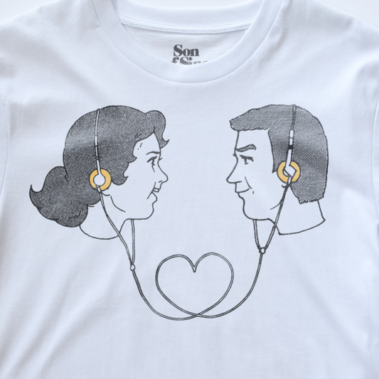 White electronic music t-shirt featuring a graphic print of a retro couple in profile facing each other, wearing headphones that form a heart shape with the earphones. 