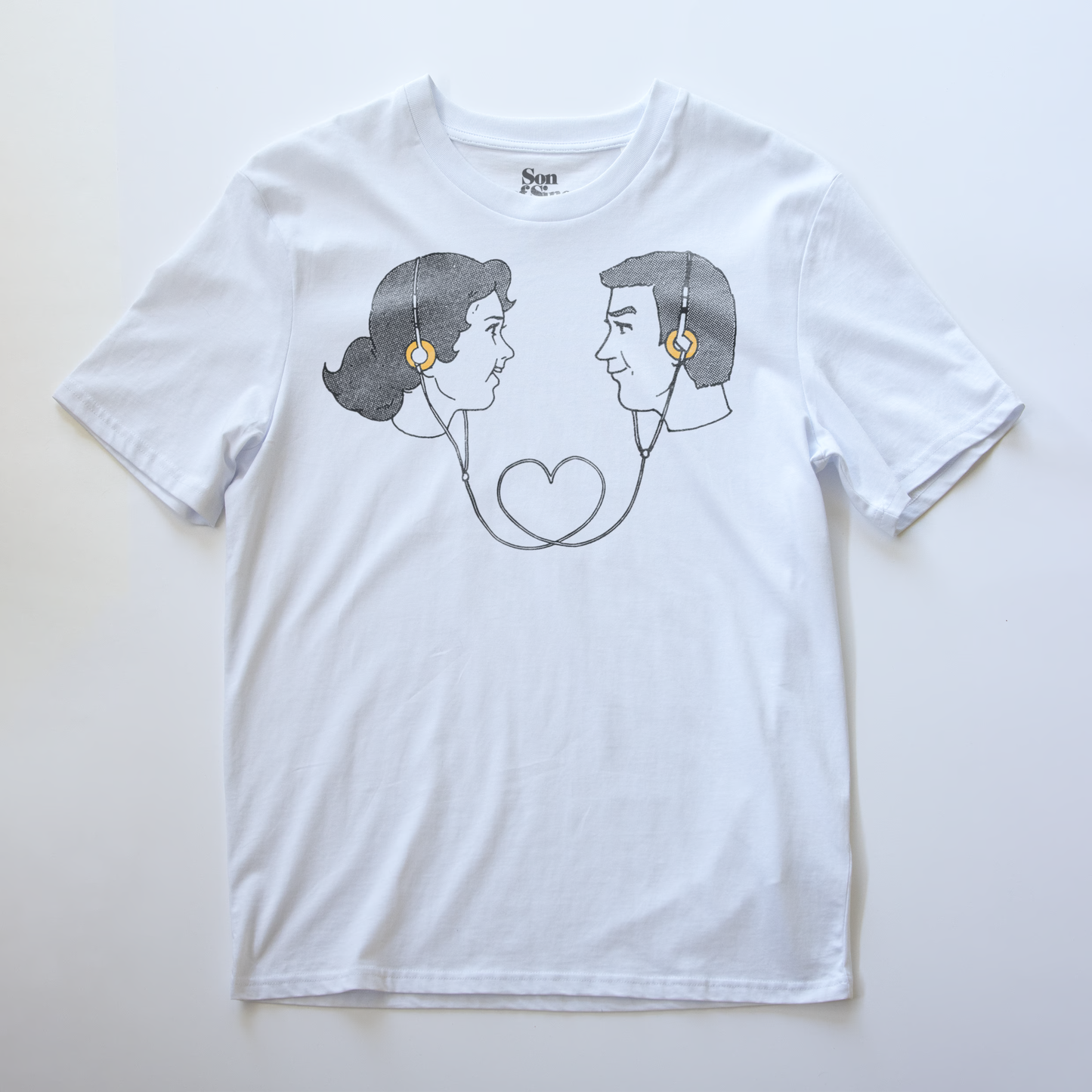 A white electronic music t-shirt with a graphic print of a retro couple facing each other wearing headphones connecting them. 