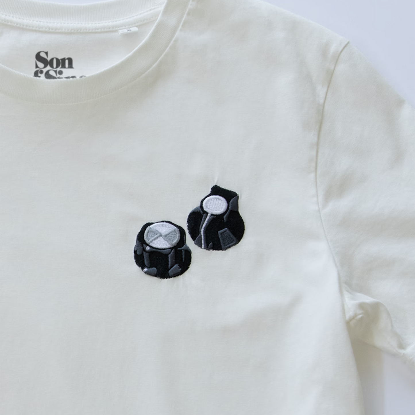 Close-up of an off-white synth T-shirt with two embroidered black Moog style controller knobs.