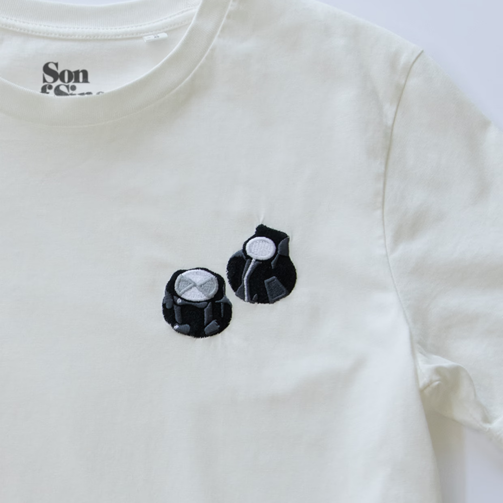 Close-up of an off-white synth T-shirt with two embroidered black Moog style controller knobs.