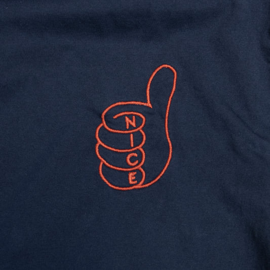 Close-up of a navy blue fabric surface with an orange embroidered outline of a thumbs-up hand and the word 'NICE' stacked inside the fingers.
