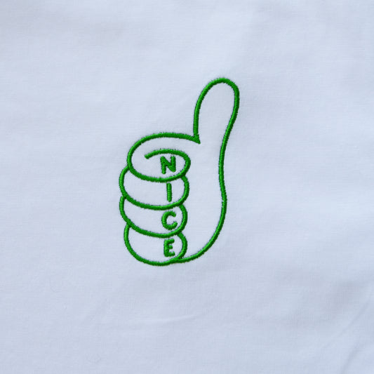 A close-up of a white fabric surface featuring a green embroidered design of a thumbs-up hand with the letters 'N', 'I', 'C', 'E' stacked inside the fingers, spelling 'NICE'.