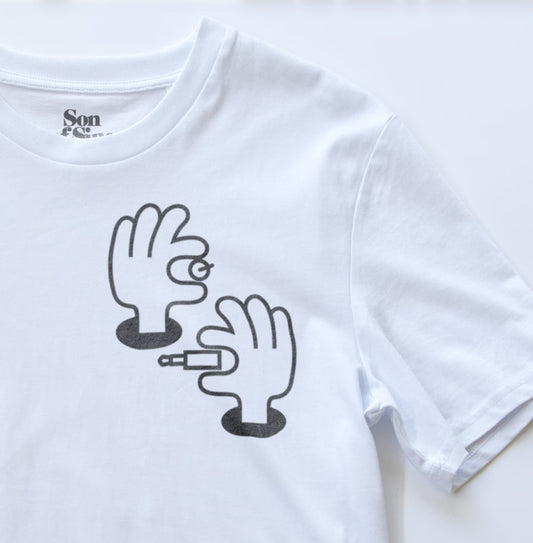 A close-up of a white modular synth t-shirt featuring a black graphic print of two cartoon hands.