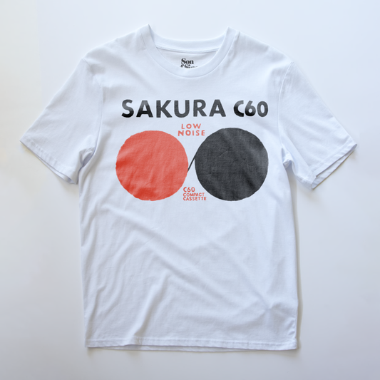 A white electronic music t-shirt with a graphic print on the front. The design features the text 'SAKURA C60' in black, with 'LOW NOISE' and 'C60 COEXIST' printed in red between them.