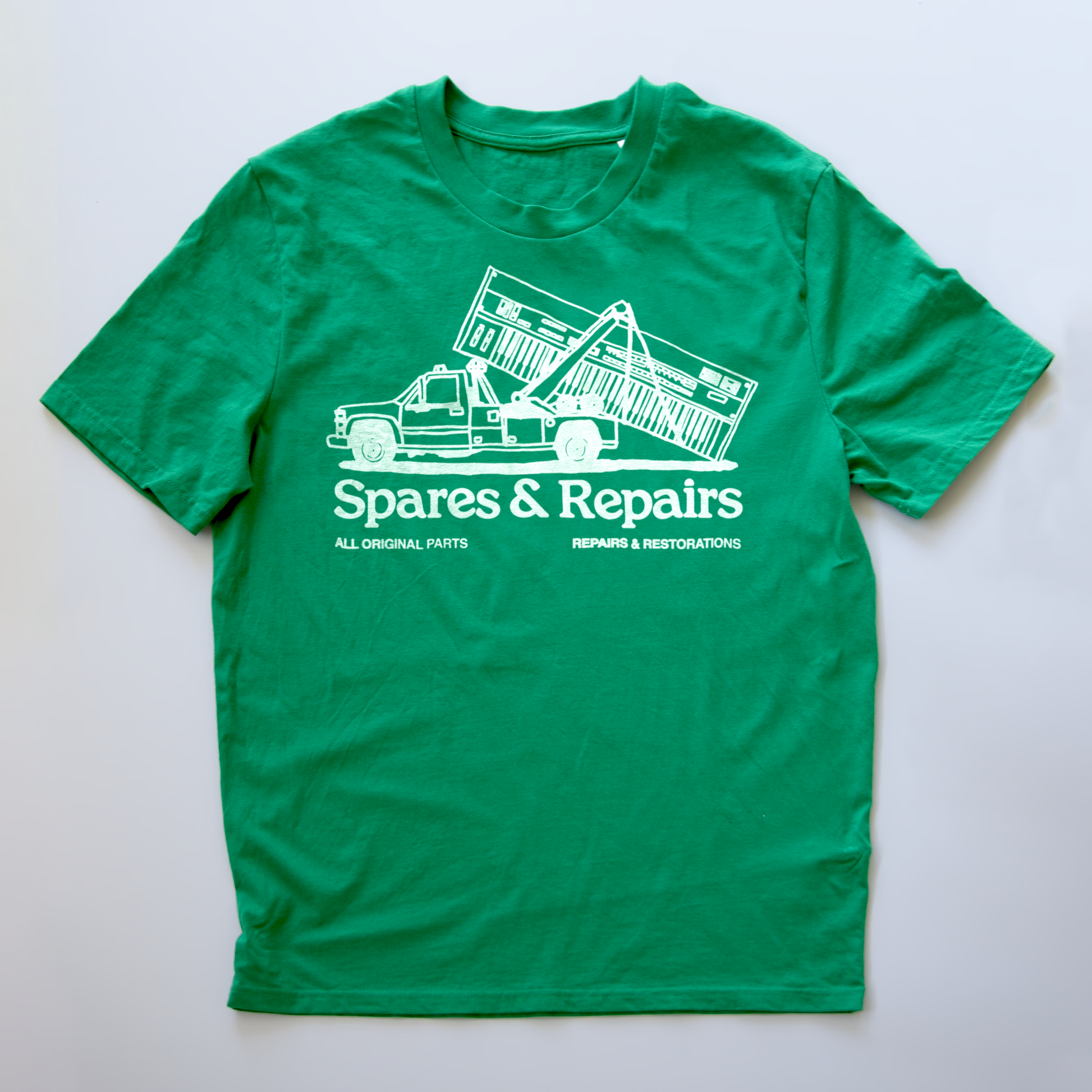 A green short-sleeve t-shirt with a white graphic print of a tow truck and the text 'Spares & Repairs' on a light gray background.