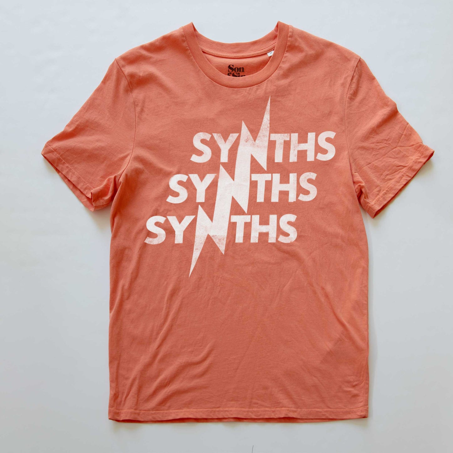 A coral orange synth inspired t-shirt featuring a distressed white graphic print of the word 'SYNTHS' repeated vertically with a lightning bolt cutting through the center.