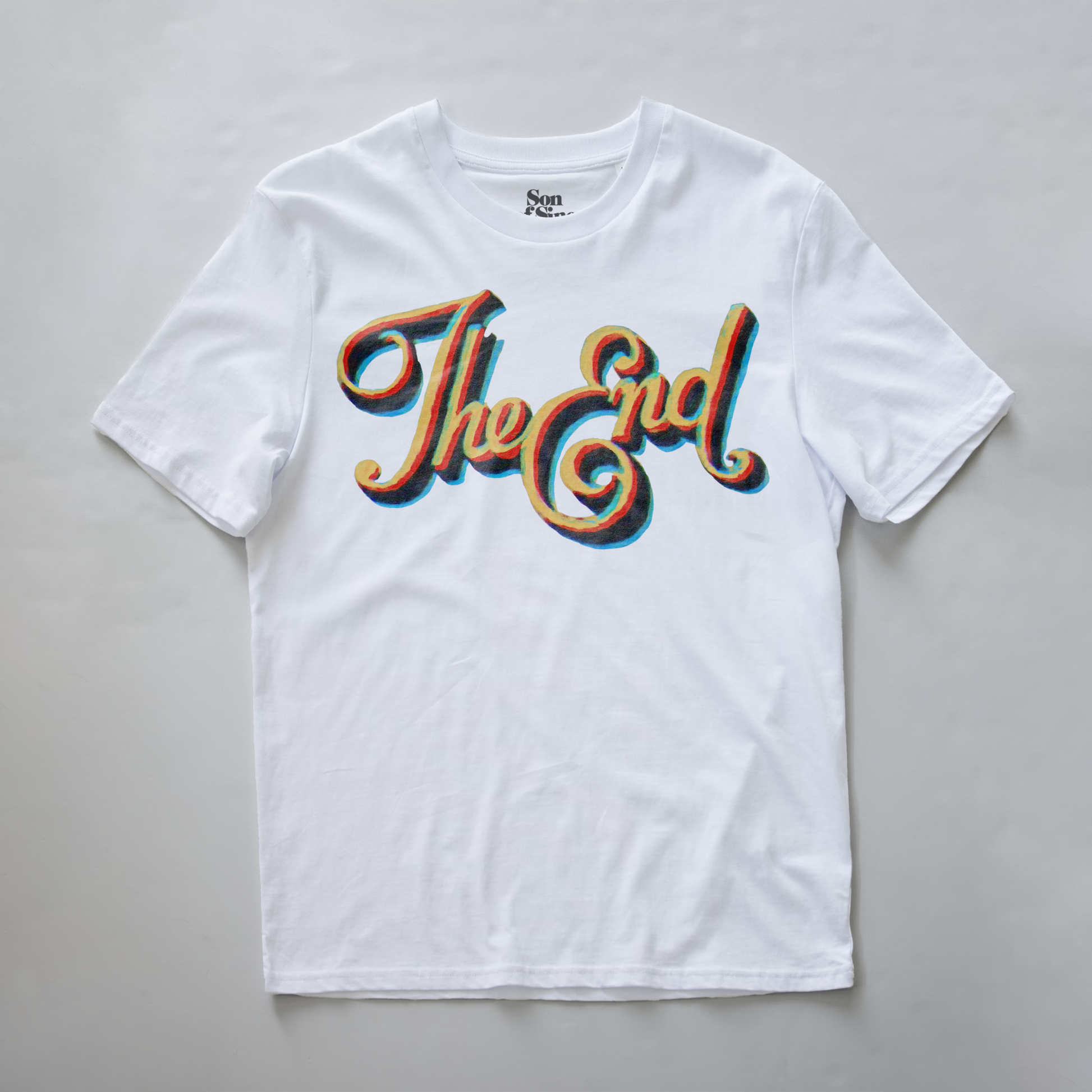 A white electronic music festival t-shirt with a retro-style graphic reading 'The End' in a wavy, layered 3D font with red, orange, and blue shadow effects.