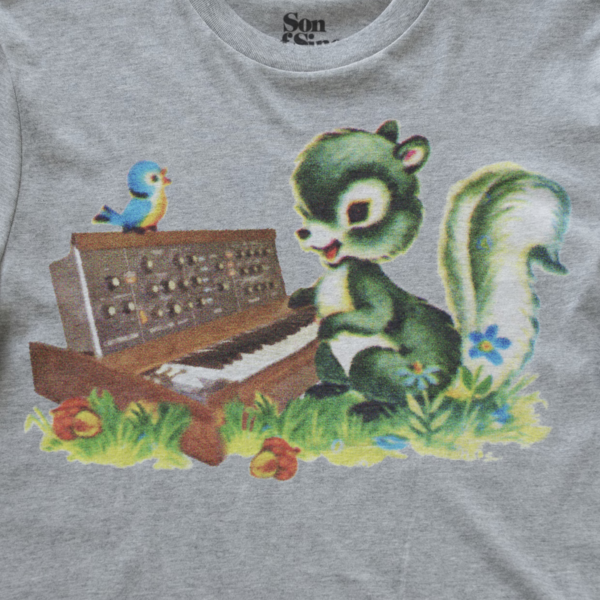 A close-up of a heather gray synth t-shirt featuring a colorful graphic print of a green squirrel playing a minimoog synthesizer keyboard, with a small blue and yellow bird perched on the keyboard and flowers in the grass.